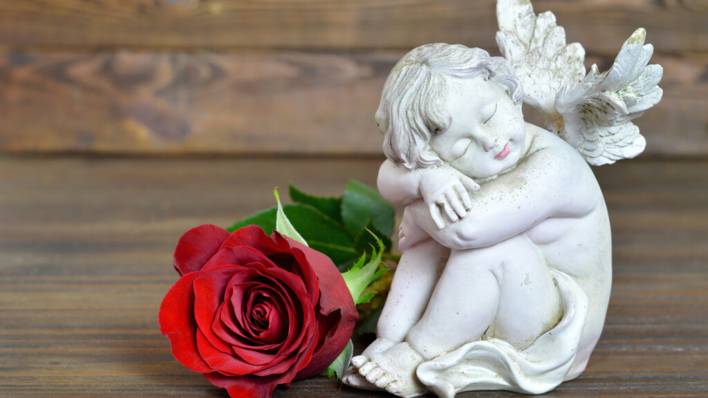 A small figurine of an angel next to a red rose.